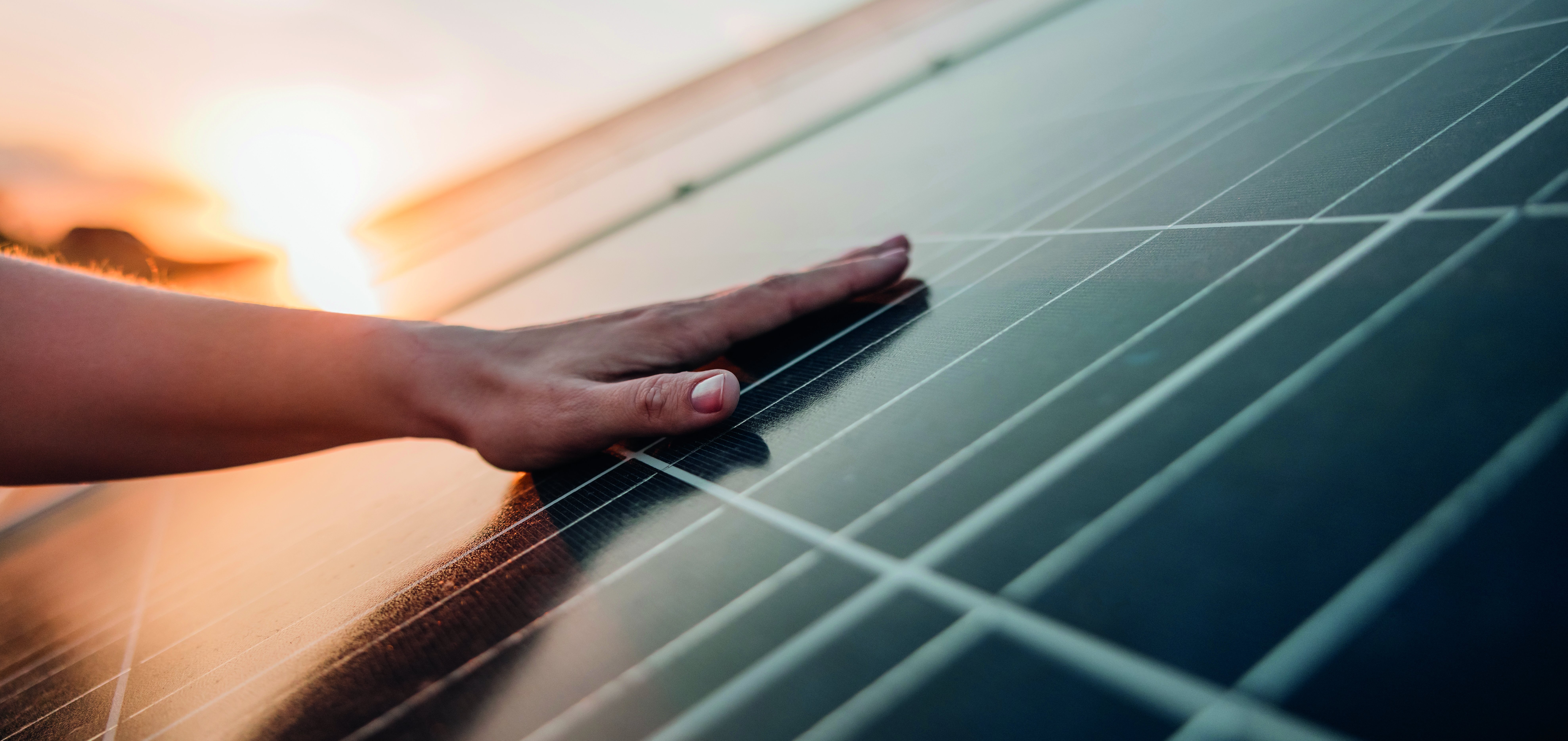 Hand berührt Solarmodul einer PV-Anlage im Sonnenuntergang