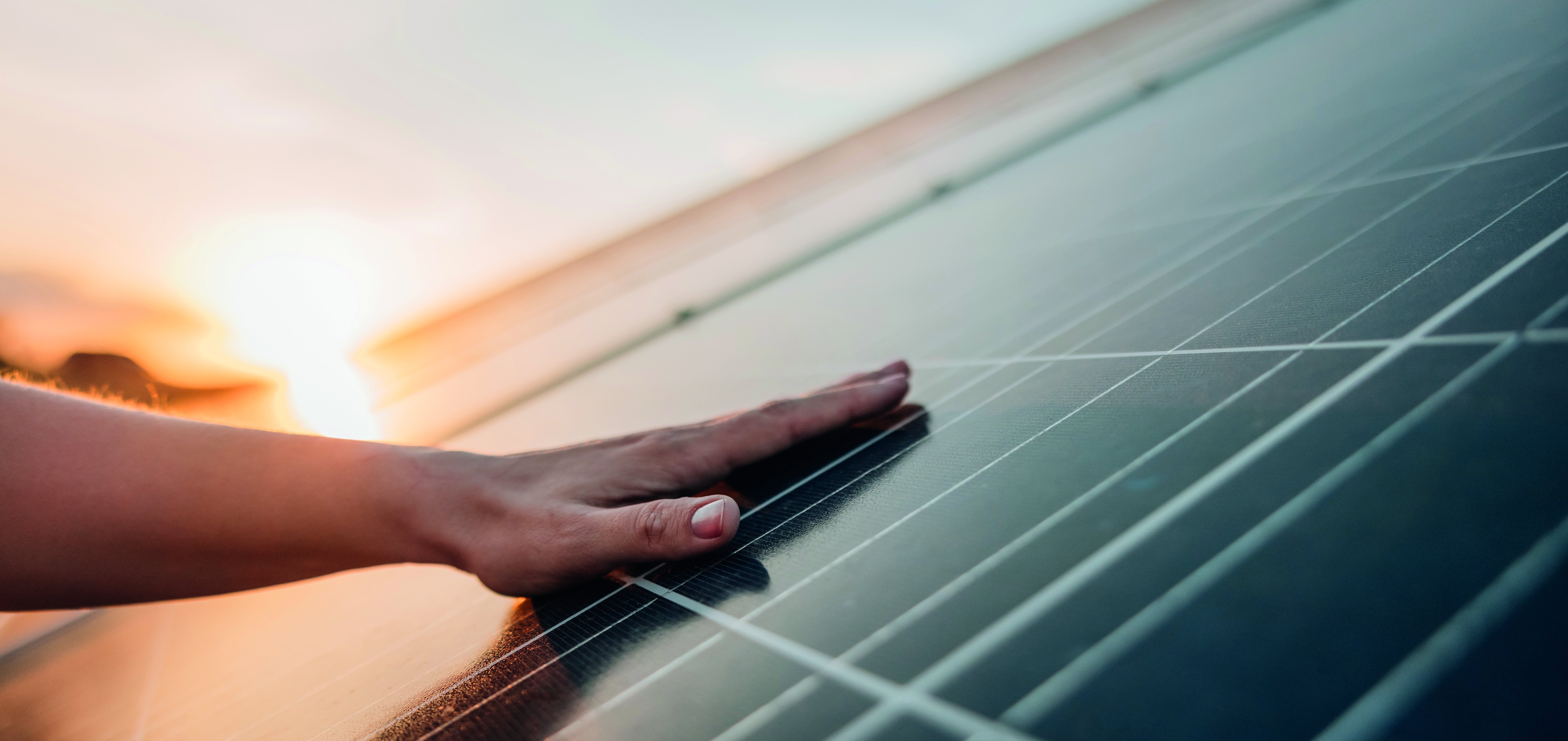 Hand berührt Solarmodul einer PV-Anlage im Sonnenuntergang